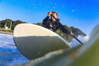 Low angle view of man splashing water against clear blue sky