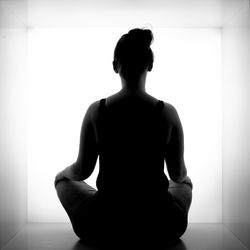 Rear view of silhouette man sitting against wall at home