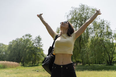 Young woman with arms raised standing against sky
