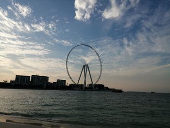 Ferris wheel by sea against sky