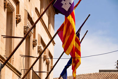 Low angle view of flags hanging on building against sky, catalonia, barcelona 