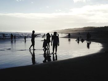 Silhouette people at beach against sky