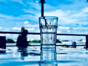 Close-up of drinking glass on table against cloudy sky 