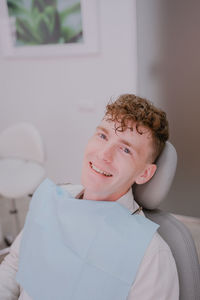 Portrait of a happy patient in the dental chair. a teenage boy with curly hair looks at the camera a