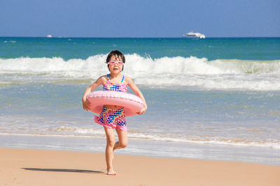 Full length portrait of girl with inflatable ring walking at beach