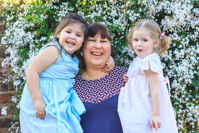 Portrait of happy woman with granddaughters standing against plants