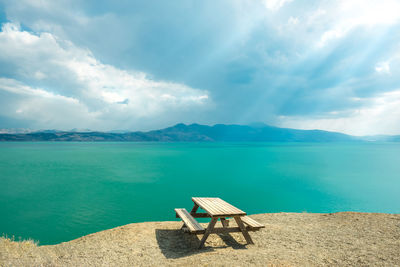 Empty chair on shore by sea against sky