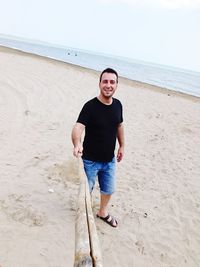 Full length portrait of happy young woman standing on beach