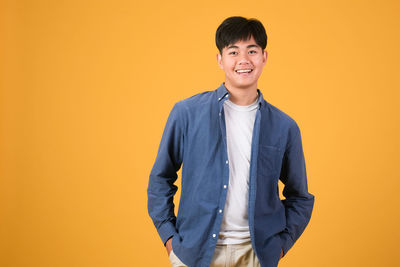 Portrait of young man standing against yellow background