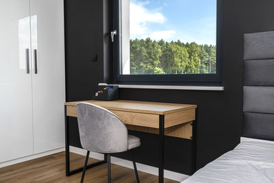 A wooden table with chair under the window in a modern boy room in black and white colors. 
