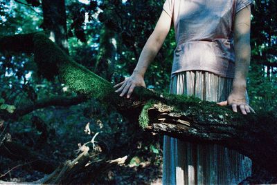 Midsection of man standing by tree in forest