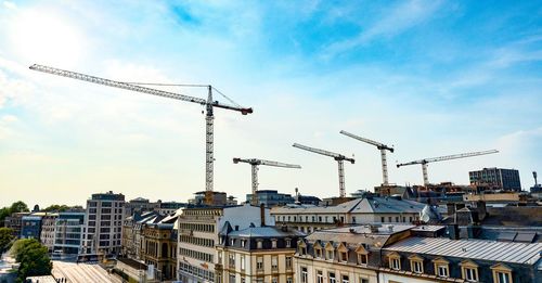 Cranes and buildings against sky in city