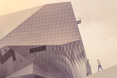 Low angle view of woman walking on building against sky