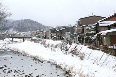 Snow covered houses by buildings against sky during winter