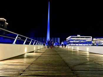 People on illuminated bridge against clear sky at night