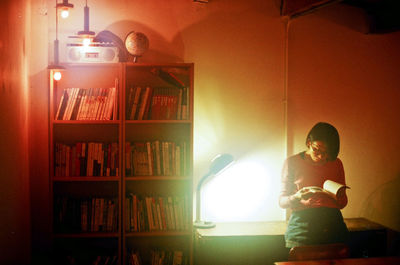 Young woman reading book in illuminated home