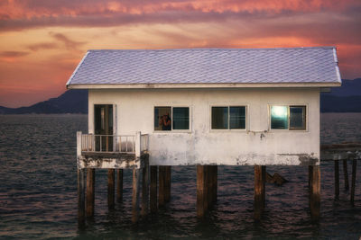 Woman standing in window of stilt house in sea during sunset