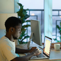 Concentrated african american man student typing email on laptop keyboard sits at office table desk.