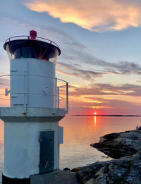 Lighthouse by sea against sky during sunset