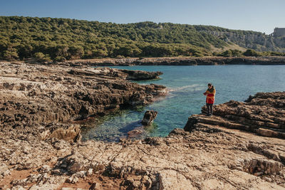 Man standing on rock formation by sea against sky