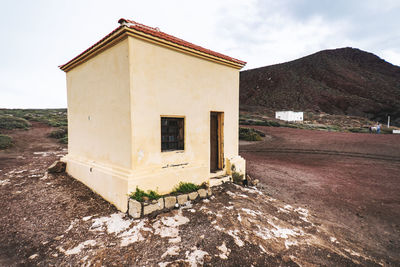 Old house on field by mountain against sky