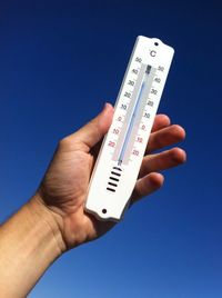 Cropped image of hand holding thermometer against clear sky