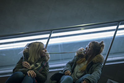 Female friends eating food while sitting on escalator