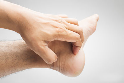 Close-up of man scratching leg against gray background