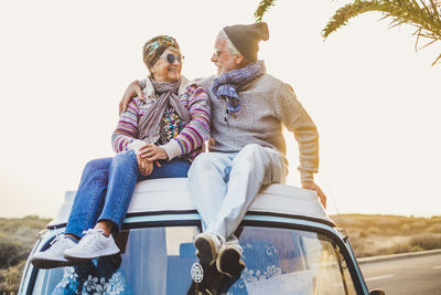 Smiling couple sitting on motor home against sky