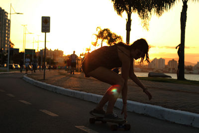 Full length of young woman skateboarding on road during sunset