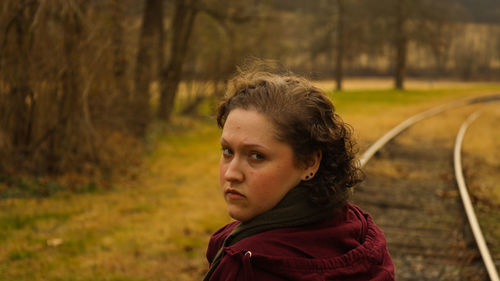 Portrait of young woman looking behind her with a solemn expression, railroad tracks behind her 