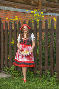 Portrait of young woman standing on wooden gate