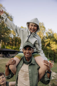 Portrait of male counselor carrying cheerful boy on shoulders while enjoying in playground