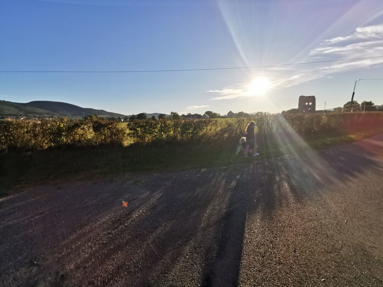 sky, horizon, landscape, nature, road, sunlight, transportation, morning, environment, lens flare, sun, land, hill, sunbeam, scenics - nature, field, plant, outdoors, rural area, beauty in nature, dusk, rural scene, day, dirt, cloud, travel, infrastructure, soil, no people, sunny, city, mode of transportation, blue