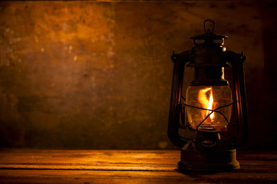 Close-up of illuminated lamp on table against wall