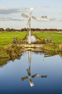 Small steel windmill reflecting in ditch in dutch polder