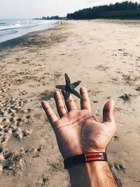 Close-up of hand holding sand at beach against sky