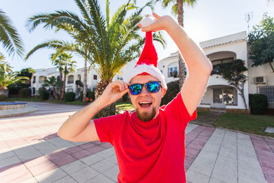 Portrait of man wearing sunglasses standing by palm trees