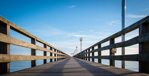 Diminishing perspective of footbridge against sky