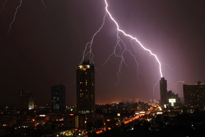 Illuminated buildings below lightning in dramatic sky at night