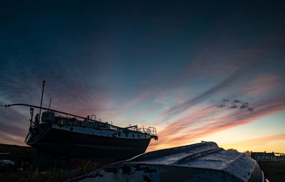 Abandoned boat moored in water against sky during sunset