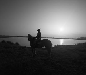 Woman riding horse at riverbank against clear sky