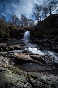 Scenic view of waterfall against sky in forest