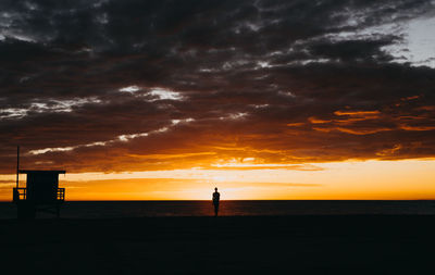 Silhouette man standing at beach against sky during sunset