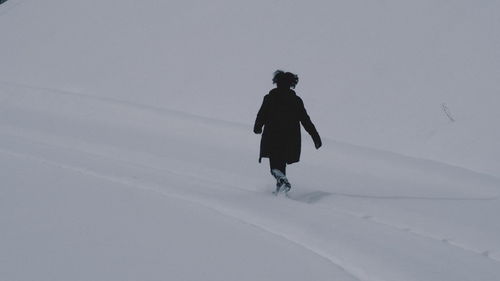 Rear view of man walking on snow covered landscape