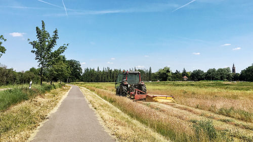 Tractor on road amidst field against sky