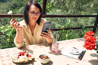 Woman cheking social media in smartphone during summer morning breakfast in cafe bar outdoors.