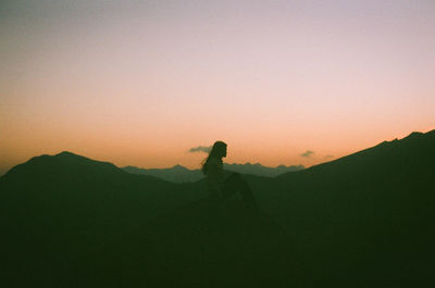 Silhouette woman sitting on mountain against clear sky during sunset