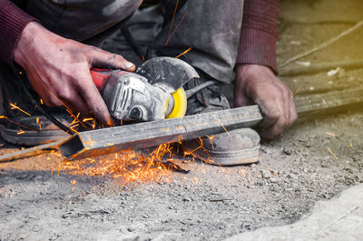 Low section of worker using power tool on metal at workshop