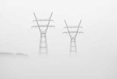 Electricity pylons on land against clear sky during foggy weather